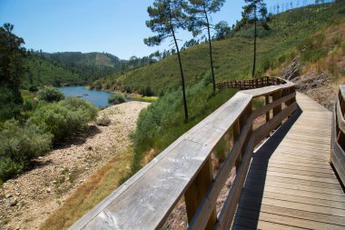 Yeşil ve dağlık manzaralı ahşap bir köprü.