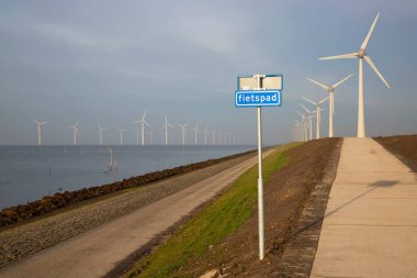 Polder hendeği yakınında temiz enerji üretimi için uzun bir sıra modern rüzgar türbinleri.