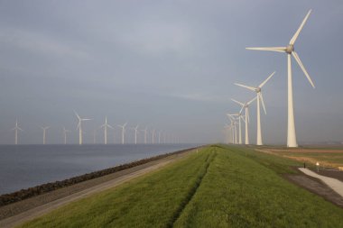 Polder hendeği yakınında temiz enerji üretimi için uzun bir sıra modern rüzgar türbinleri.