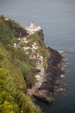 Etrafı doğal bulutlarla çevrili tarihi deniz feneri bir uçurumun tepesine ve limana uzanan dik erişim yoluna ışık hüzmesi veriyor.