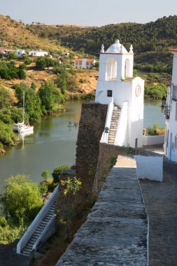 Kırsal nehir manzarası ve binalarda eski çatı kiremitleri ve tepedeki saat kulesinin yanındaki dar caddelerin bulunduğu pitoresk kasaba manzarası.