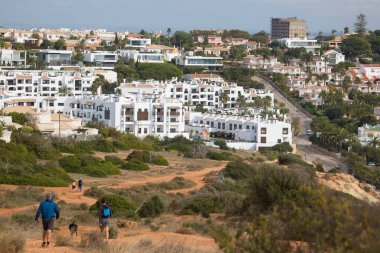 Yürüyen insanların ve arka planda küçük kasaba binalarının olduğu doğal bir sahne.