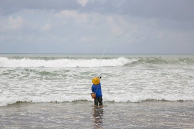 Sahilde şapkalı bir adam balık tutuyor.