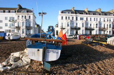 Tekneler kıyıya demirlemiş binalar ve mavi gökyüzü arka planda.