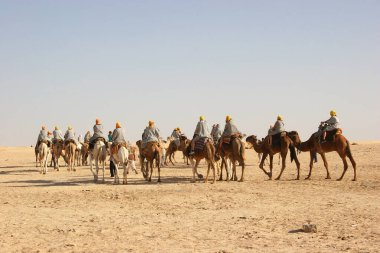 Çölde develerin üzerinde gezen insanların manzarası.
