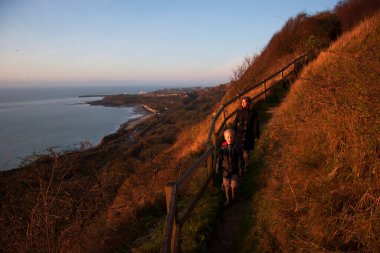 Bir çift yürüyüşçü, deniz kenarındaki tepede yürüyor. Folkestone 'ların siperlerindeki sahil şeridinde.