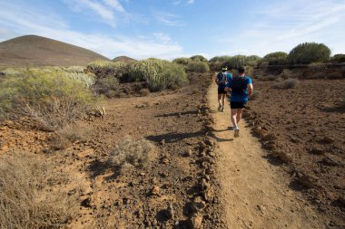 Deniz kenarındaki kayalık bir yolda yürüyen turistlerin görüntüsü