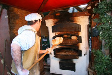 Adam hamuru fırına koyuyor, ekmek pişiriyor.