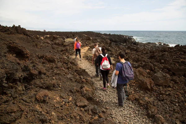 Deniz kenarındaki kayalık bir yolda yürüyen turistlerin görüntüsü