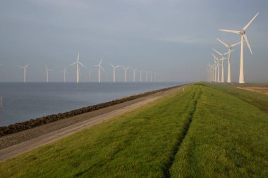 Polder hendeği yakınında temiz enerji üretimi için uzun bir sıra modern rüzgar türbinleri.