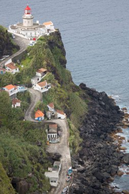 Etrafı doğal bulutlarla çevrili tarihi deniz feneri bir uçurumun tepesine ve limana uzanan dik erişim yoluna ışık hüzmesi veriyor.