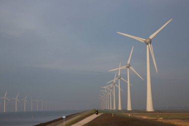 Polder hendeği yakınında temiz enerji üretimi için uzun bir sıra modern rüzgar türbinleri.