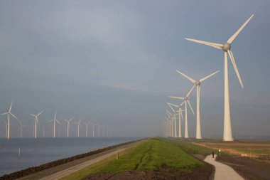 Polder hendeği yakınında temiz enerji üretimi için uzun bir sıra modern rüzgar türbinleri.