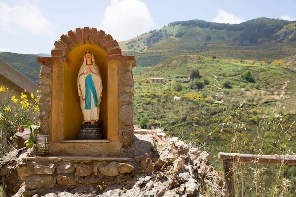 Arka planda yeşil tepeler olan Aziz Maria heykeli