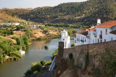 Kırsal nehir manzarası ve binalarda eski çatı kiremitleri ve tepedeki saat kulesinin yanındaki dar caddelerin bulunduğu pitoresk kasaba manzarası.