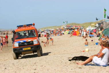 Kurtarma ekibi arabası ve halk plajında dinlenen insanlar.