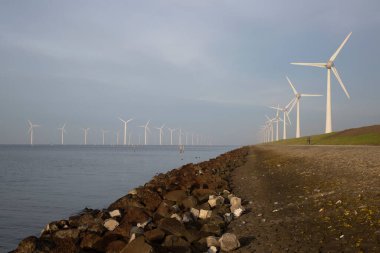 Polder hendeği yakınında temiz enerji üretimi için uzun bir sıra modern rüzgar türbinleri.