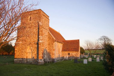 Yumuşak güneş ışığıyla aydınlatılan mezar taşlarıyla ortaçağ kilisesi ve mezarlığı