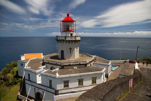 Etrafı doğal bulutlarla çevrili tarihi deniz feneri bir uçurumun tepesine ve limana uzanan dik erişim yoluna ışık hüzmesi veriyor.