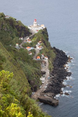 Etrafı doğal bulutlarla çevrili tarihi deniz feneri bir uçurumun tepesine ve limana uzanan dik erişim yoluna ışık hüzmesi veriyor.