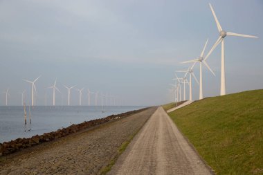 Polder hendeği yakınında temiz enerji üretimi için uzun bir sıra modern rüzgar türbinleri.