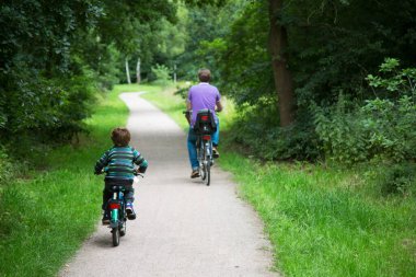 baba ve oğul parkta bisiklet sürüyorlar.
