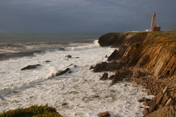 Kayalıklarla kaplı engebeli kıyı manzarası, sörf dalgaları, denizdeki kayalar, yumuşak güneş ışığıyla aydınlatılmış.