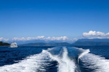 A motor yacht leaves a smooth wake as it glides through the tranquil waters of Desolation Sound British Columbia, showcasing stunning mountain scenery.