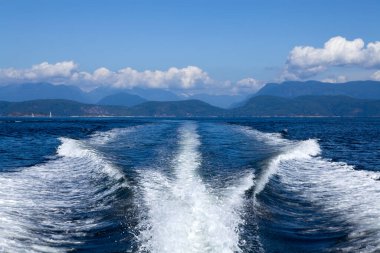 A motor yacht leaves a smooth wake as it glides through the tranquil waters of Desolation Sound British Columbia, showcasing stunning mountain scenery.