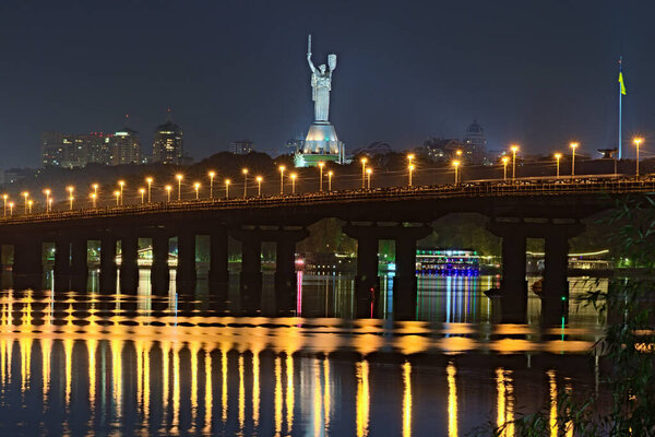 Night cityscape with Paton bridge over Dnieper river. Famous Motherland monument at the background. City lights reflected in the water. Kyiv, Ukraine.