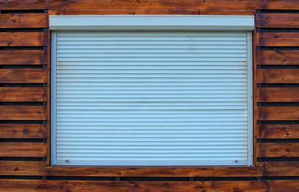 Sample of white window roller shutters. White horizontal metal strips. Closed metal shutter casements. Protecting windows from intruders. White window roller shutters in a wooden wall.