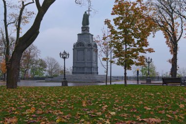 Görkemli sonbahar renkleri olan Volodymyr Tepesi 'nin (β mirskaya Girka) alçak açılı görüntüsü. Yeşil çimlerde düşen portakal yaprakları. Volodymyr 'in ünlü anıtı. Arka planda ağaçlarla çevrili..