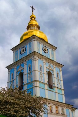 Kyiv 'deki ünlü Aziz Michael Altın Kubbe Manastırı' nın çan kulesinin manzarası. Kulenin yanında bir sürü çiçek açan bir ağaç. Arka planda bulutlu mavi gökyüzü