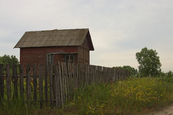 Malý starý dům s plotem na okraji pole — Stock fotografie