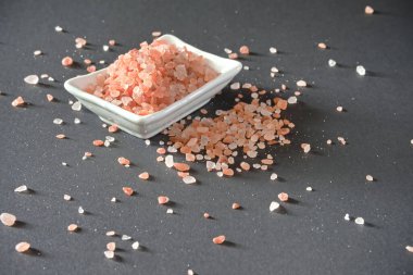 Masaya dökülen beyaz bir kasede pembe Himalaya tuzu. Bir tuz kristalinin dokusuna yakın çekim
