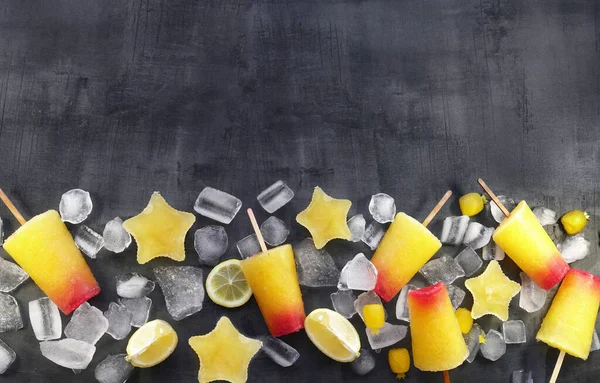 Sweet refreshing summer food concept. Summer ice cream fruit ice stars yellow orange and red colors and slices of lemon top view on dark background of table, free copy space.