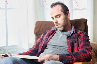 Adam pencerenin yanındaki kanepede kitap okuyor.