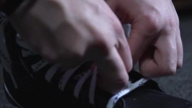 Soyunma odasında beyaz ayakkabı bağcıklarıyla siyah paten bağlayan adam.