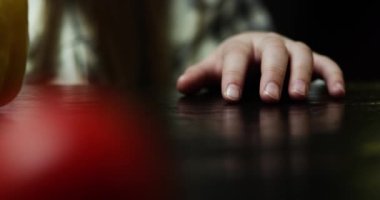 Çocuk eli gergin bir şekilde masaya vurur. Ön planda odaktan çıkmış bir domates.