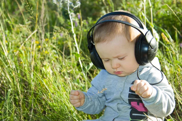 A little boy sits on a meadow with headphones — Stock Photo, Image
