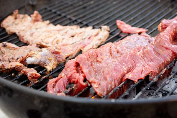 A view of cuts of beef sirloin flap cooking on a kettle grill.