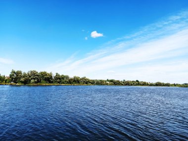 Güzel bir manzara, nehrin su yüzeyi, mavi gökyüzü, uzakta beyaz bulutlar ve ormanlar, karşı tarafta.