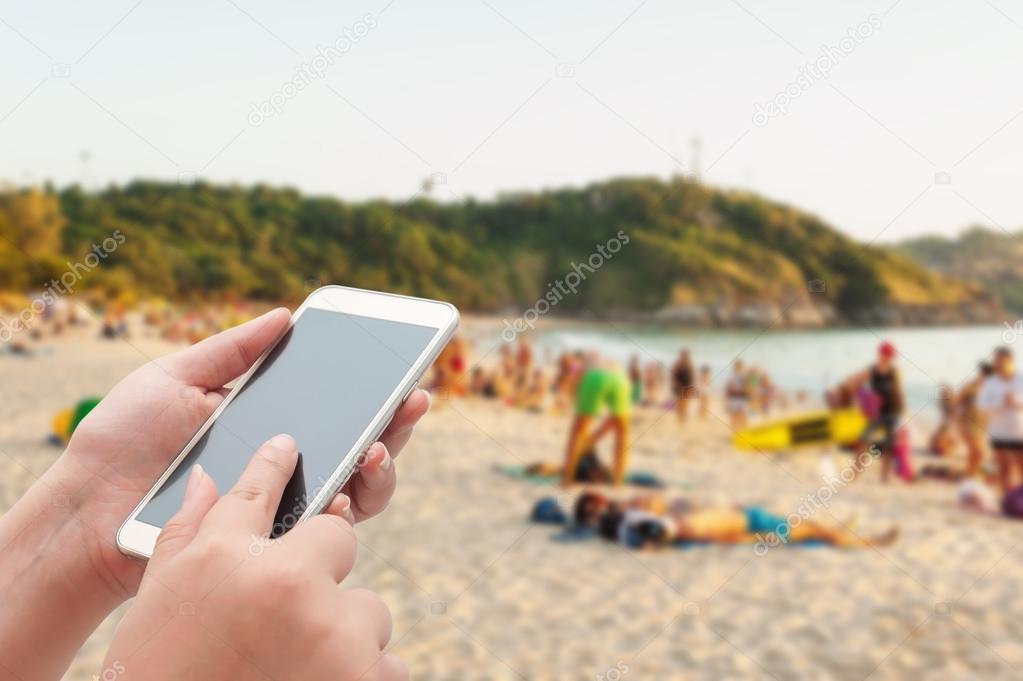 Women using smartphone top on blurred sea and sand beach with so