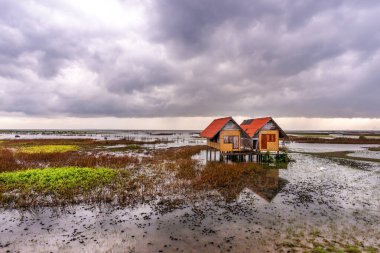 Gölün ortasında terk edilmiş bir evin görüntüsü. Gün batımında gökyüzü ve bulut yağmuru.