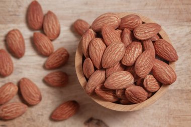 Bademler ahşap bir fincanda ve doğal bir ahşap tabakta, basit organik dokuları vurguluyor..