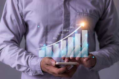 Akıllı telefon elli genç adam para büyümesini görselleştirmek için dokunuyor telefon ekranında artan yatırım ve tasarruf eğilimlerinin yanı sıra artan bir hesap dengesi gösteren grafikler ve grafikler gösteriliyor