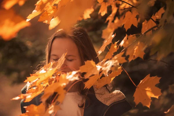 A 10-year-old girl walks in the park in a green coat in autumn.Yellow leaves, a beautiful girl on a walk. Long hair, a smile. Warm orange background.