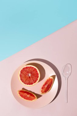 Plastik kaşıkta taze greyfurt dilimleri olan bir yaz sahnesi. Kopya alanı ile asgari estetik plaj kavramı.