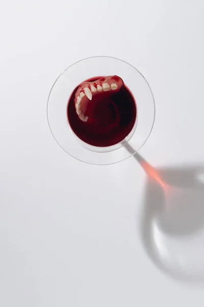 Martini glass with Vampire Teeth and blood against bright background. Minimal Halloween concept with copy space. Flat lay.