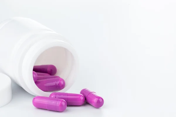 Pílulas roxas uma garrafa pílula no backgroun branco — Fotografia de Stock